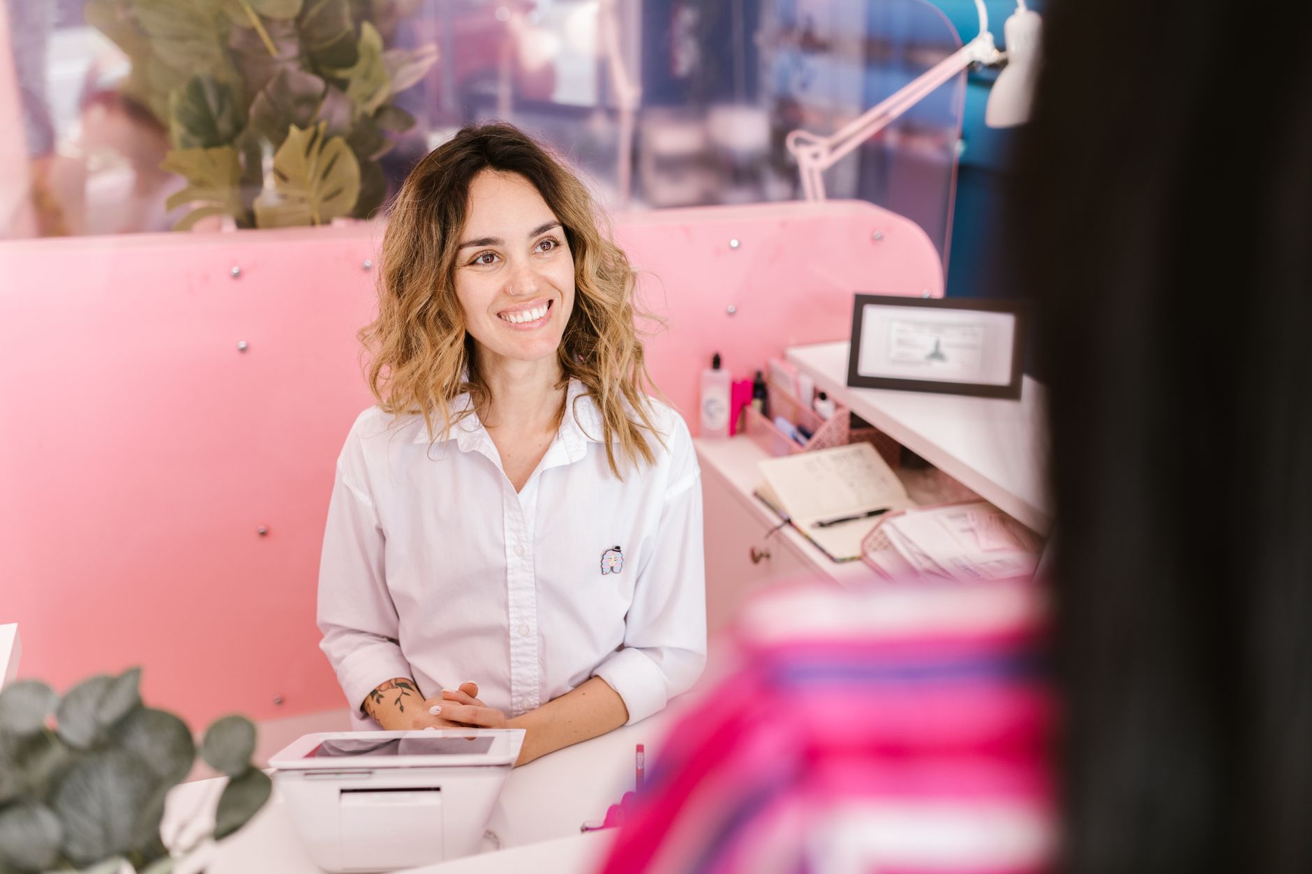 Smiling receptionist at a salon front desk, welcoming clients with a friendly demeanor.