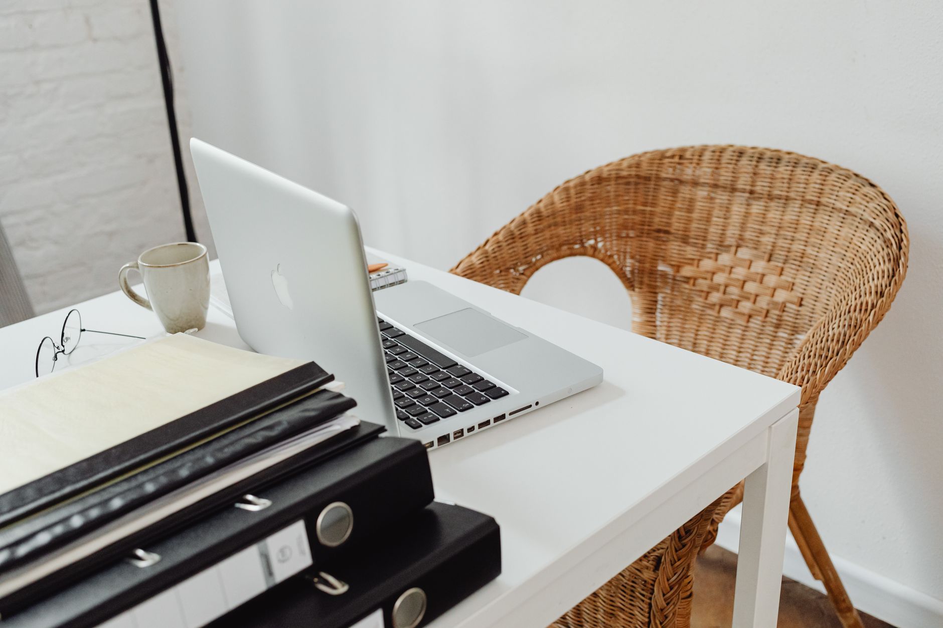 A cozy home office setup featuring a laptop, binders, and wicker chair for productive remote work.